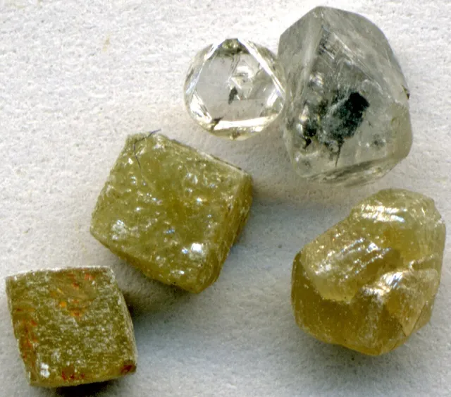 Cinco diamantes africanos recién sacados de la mina. Fíjate en que todos tiran a la misma forma: es la red la que manda, igual que en los cubos de la sal.
